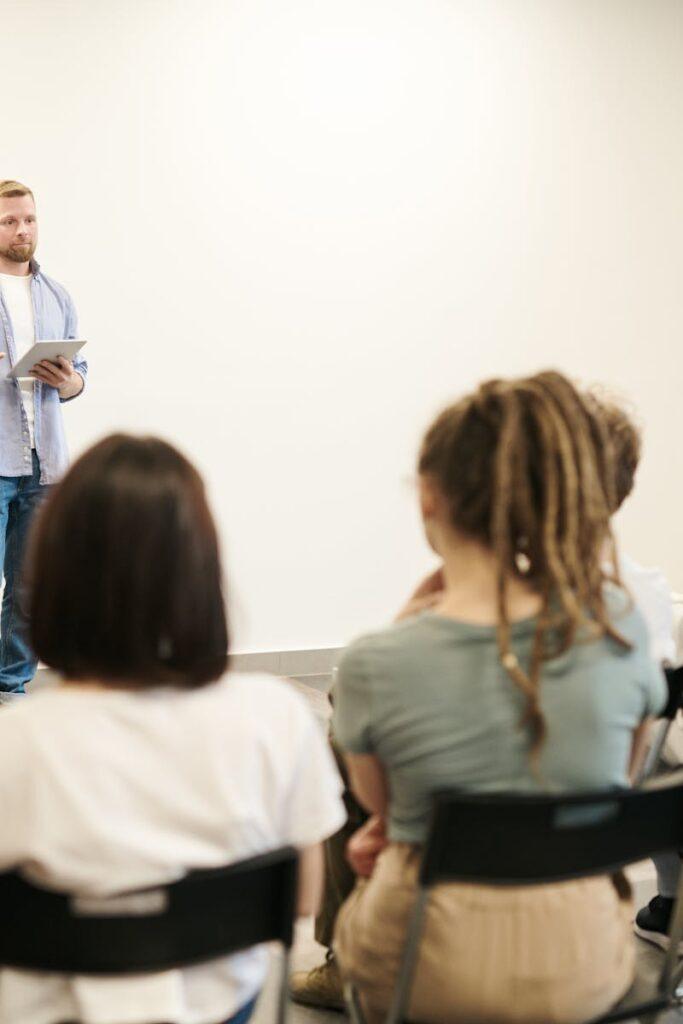 Man presenting with tablet to a small seated audience in a modern indoor setting.