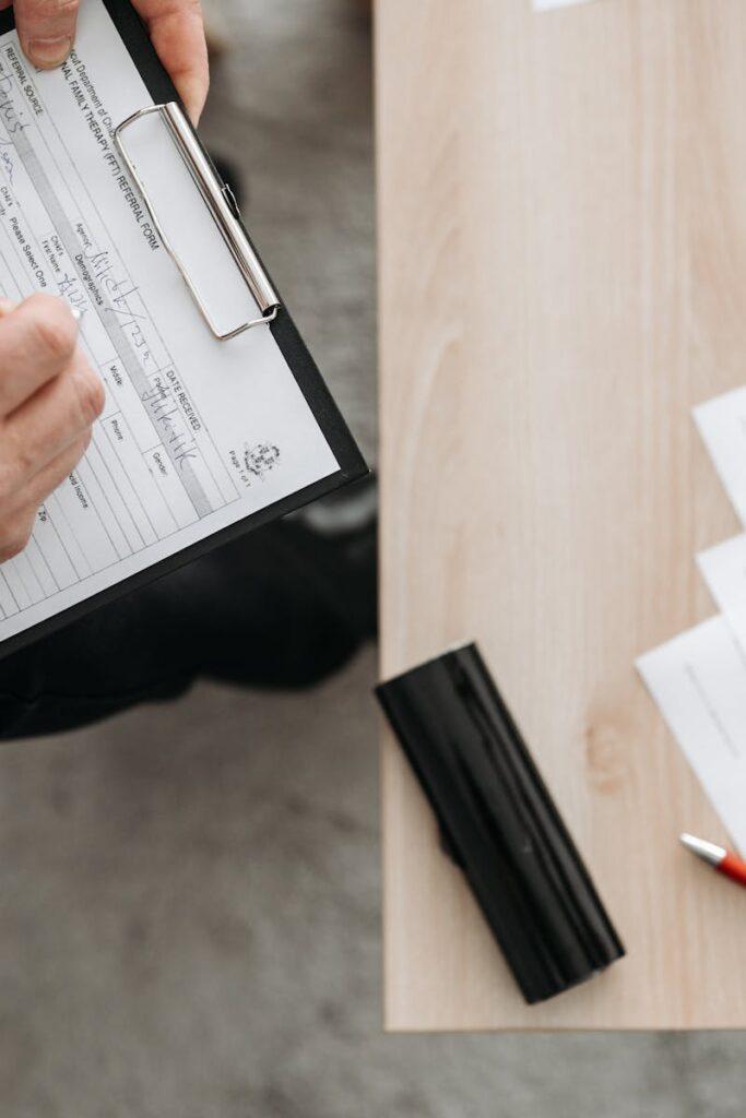 High-angle view of a person filling out forms on a clipboard, emphasizing paperwork and documentation.